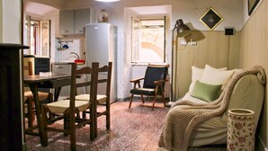 Una sala de estar acogedora con sofá, sillón, mesa de comedor con sillas, zona de cocina y ventana con cortinas.