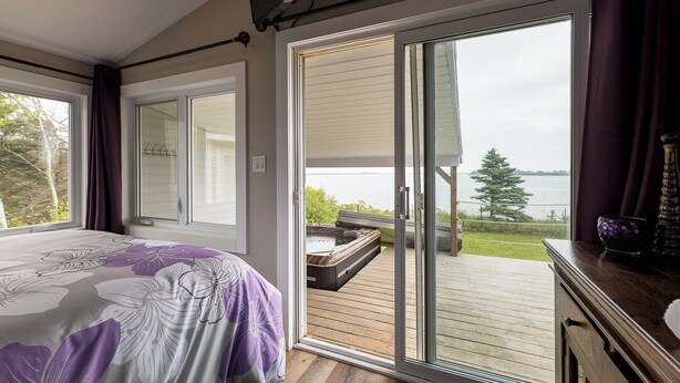 Een slaapkamer met een groot bed, een schuifdeur naar een terras en uitzicht op een waterlichaam.