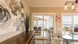 Een modern interieur met een glazen eettafel, witte stoelen, een houten bank en een groot abstract schilderij aan de muur.