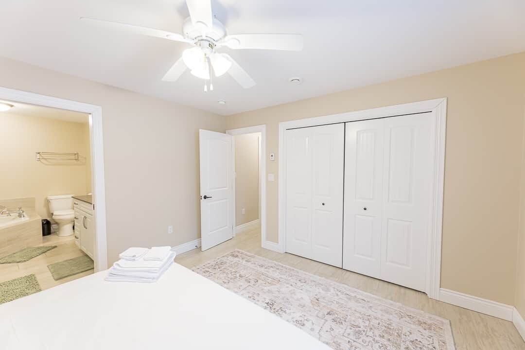 Une chambre à coucher comprenant un lit, un ventilateur de plafond, un dressing et une salle de bain avec des toilettes et un lavabo.