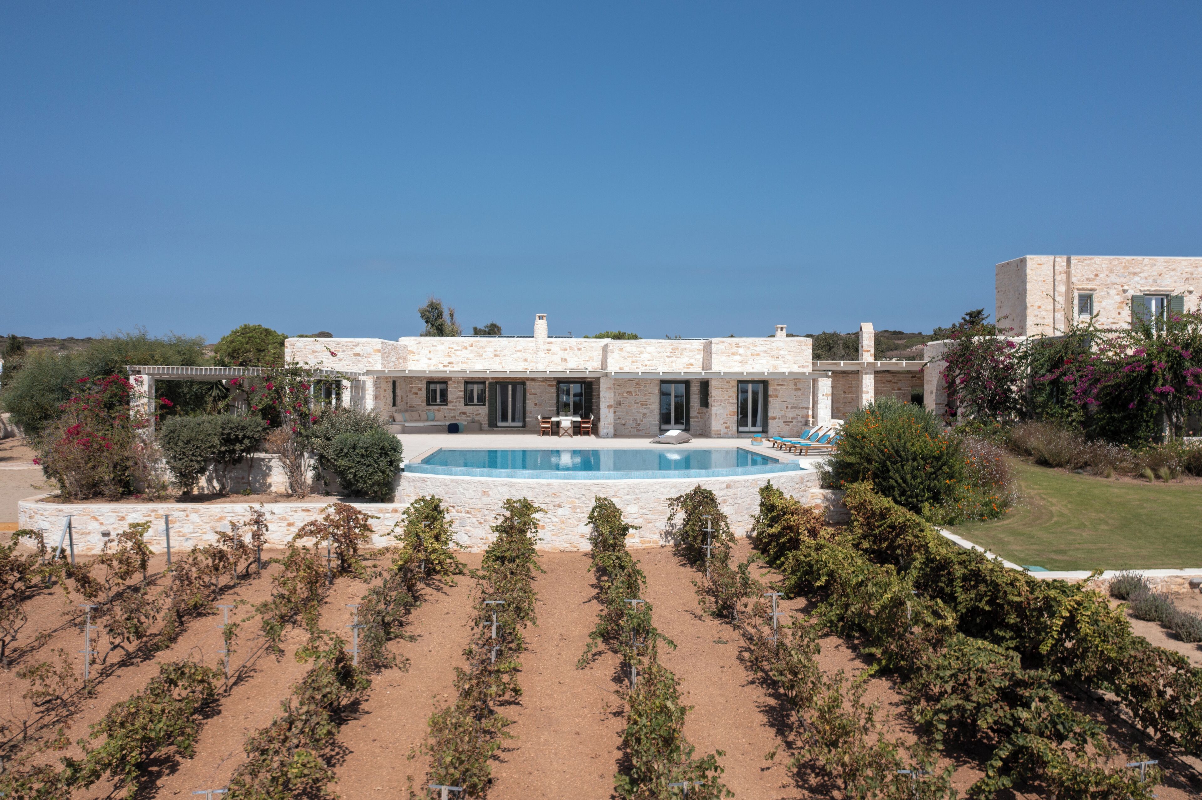 A large house with a swimming pool, surrounded by a garden and vineyard.