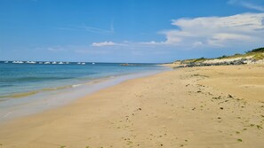 A sandy beach with calm waters, boats in the distance, and a rocky shoreline. - Les Malouines, a beachfront vacation home on the island of Oléron with a pool (Saint-Pierre-d'Oléron)