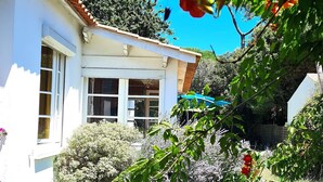Une maison blanche avec un toit en tuiles, entourée d’une végétation luxuriante et de plantes en fleurs.