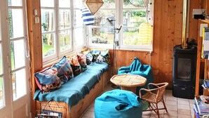 L’intérieur chaleureux d’un chalet avec un banc intégré le long de la fenêtre, une table ronde en osier et un poêle à bois noir.