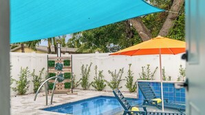 En swimmingpool med et hvidt hegn, en blå og orange parasol samt en metalstige.