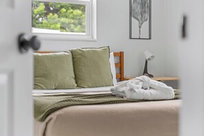 A bedroom with a bed, pillows, a bedside table with a lamp, and a window with a view of greenery. - Heated Salt Pool and Spa, Sleeps 8, 8 Minutes to the Beach (Pompano Beach)