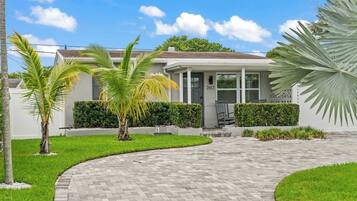 A residential house with a paved driveway, palm trees, and a well-maintained lawn.
