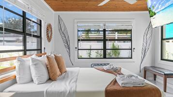 A bedroom with a bed, a bench, a ceiling fan, and a window with a view of greenery.
