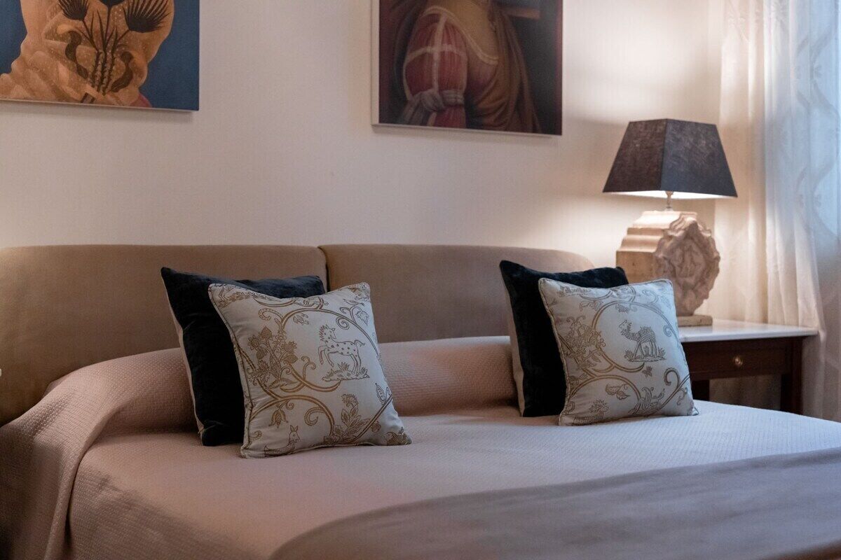 Ein Hotelzimmer mit einem Bett, zwei Zierkissen, einem Nachttisch mit Lampe und Wandbildern.