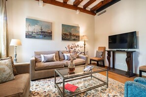 A living room with a sofa, armchairs, a coffee table, a TV, and artwork on the walls. - Ca' Barbarina 1 (Venezia)