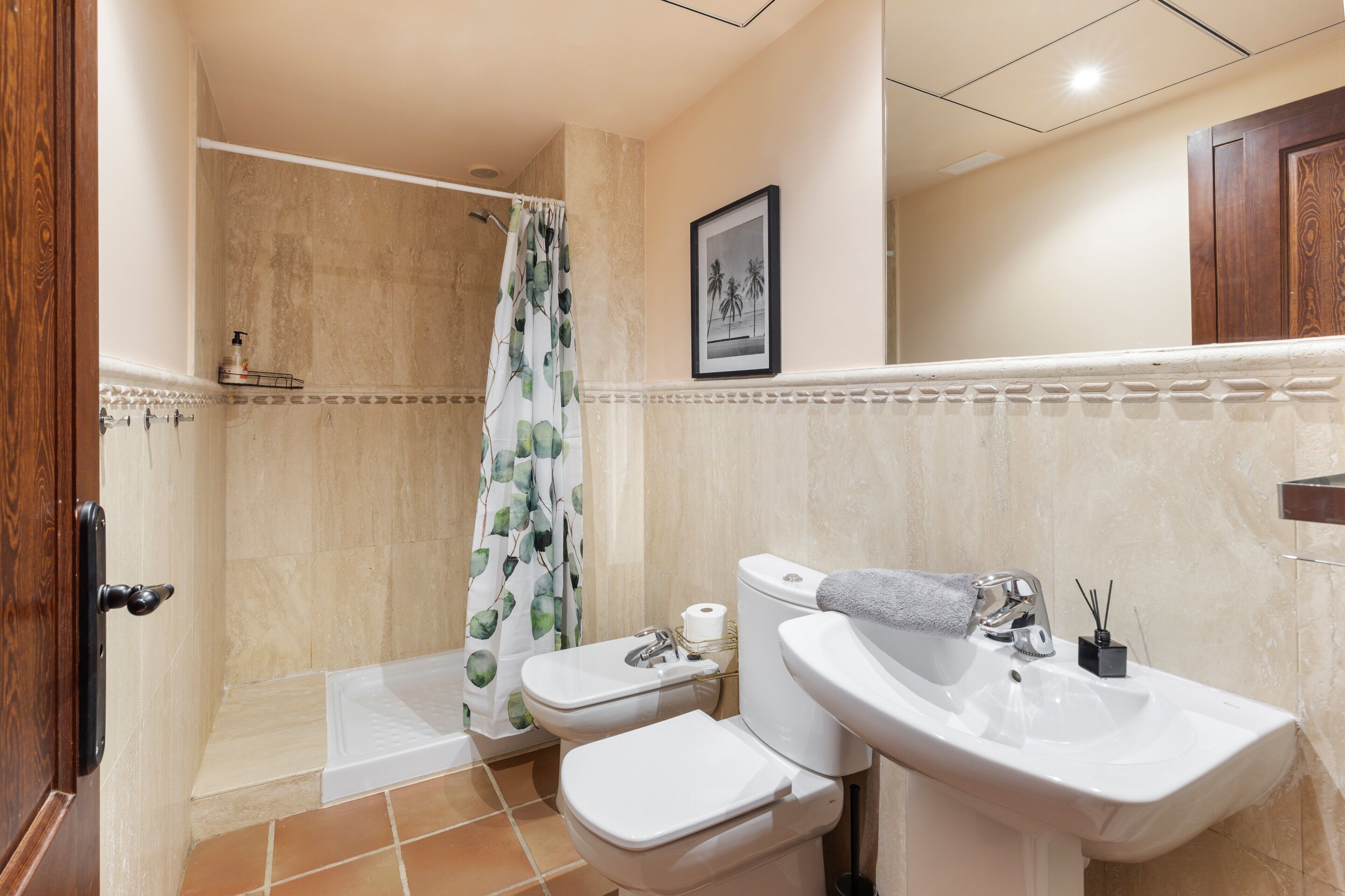Ein Badezimmer mit Dusche, zwei Toiletten, einem Waschbecken und einem gerahmten Bild an der Wand.