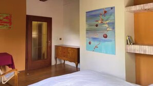 Ein Schlafzimmer mit einem Bett, einer Holzkommode, einer Tür mit Glasverzierungen und einem Wandbild.