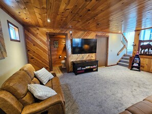 A cozy living room with a wooden ceiling, a flat-screen TV, a sofa, and a bookshelf. - 3BR Entire Home-Dog Friendly- Near DIA & Golf Course - Hot Tub (Denver)