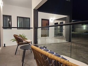 A modern balcony with a glass railing, a wicker chair, a small table, and a sofa.