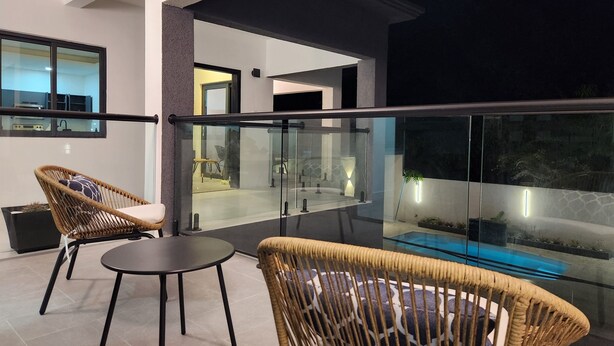 A modern balcony with wicker furniture, a glass railing, and a view of a swimming pool. - 8B/R w/pool Complex @ Terrace Eight (Kingston 6)