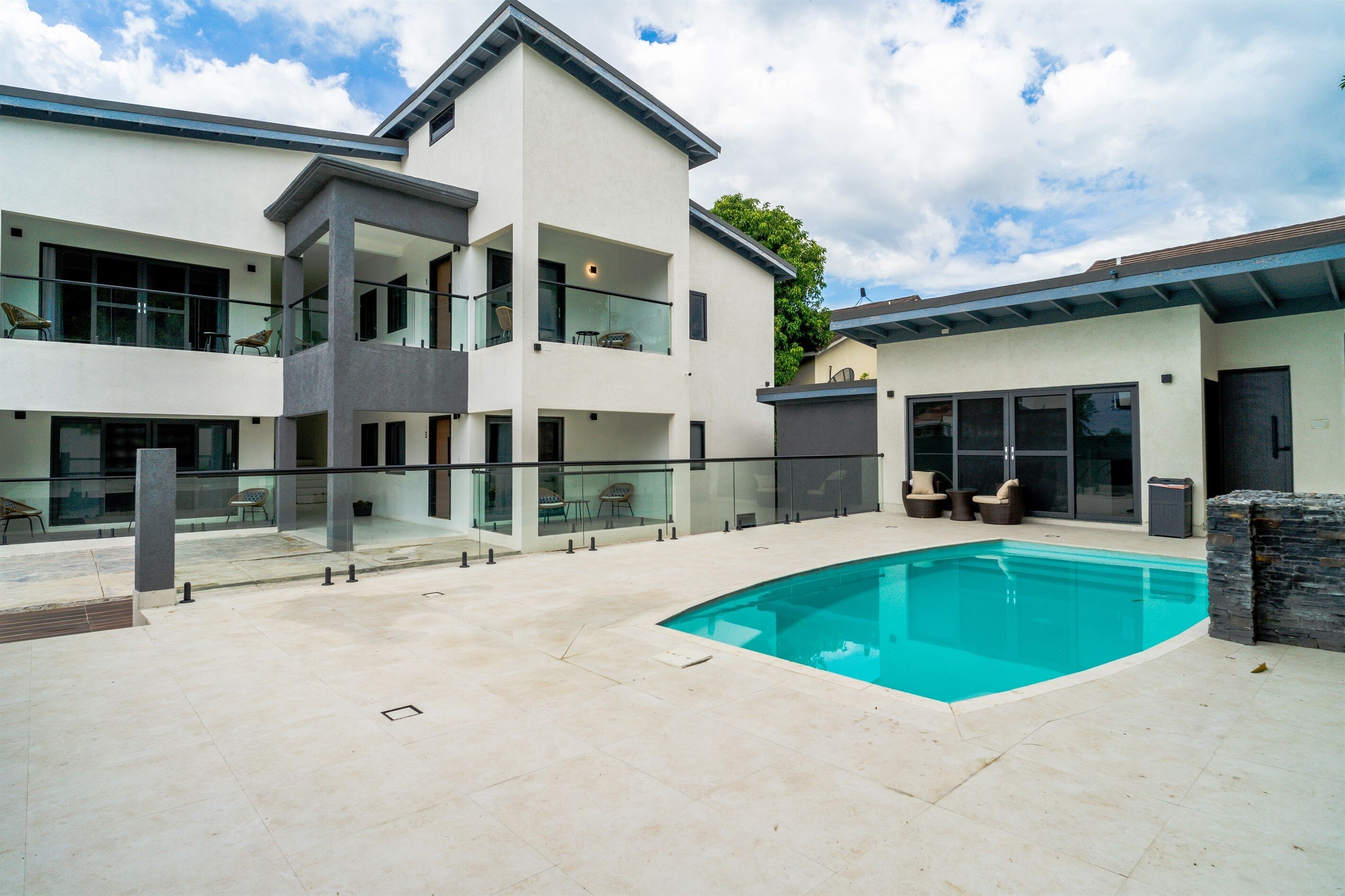 A modern two-story house with a swimming pool, glass railings, and outdoor seating.