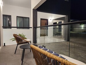 Ein moderner Balkon mit Glasgeländer, einem Korbstuhl, einem kleinen Tisch und einer Couch.