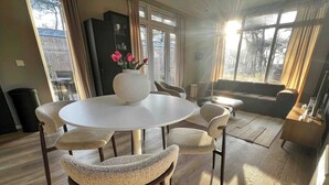 Un salon moderne avec une table ronde, des fauteuils en osier, un canapé et une grande fenêtre avec des rideaux.