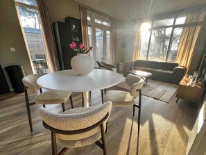 Ein modernes Wohnzimmer mit einem runden Tisch, Korbstühlen, einer Couch und einem großen Fenster mit Vorhängen.
