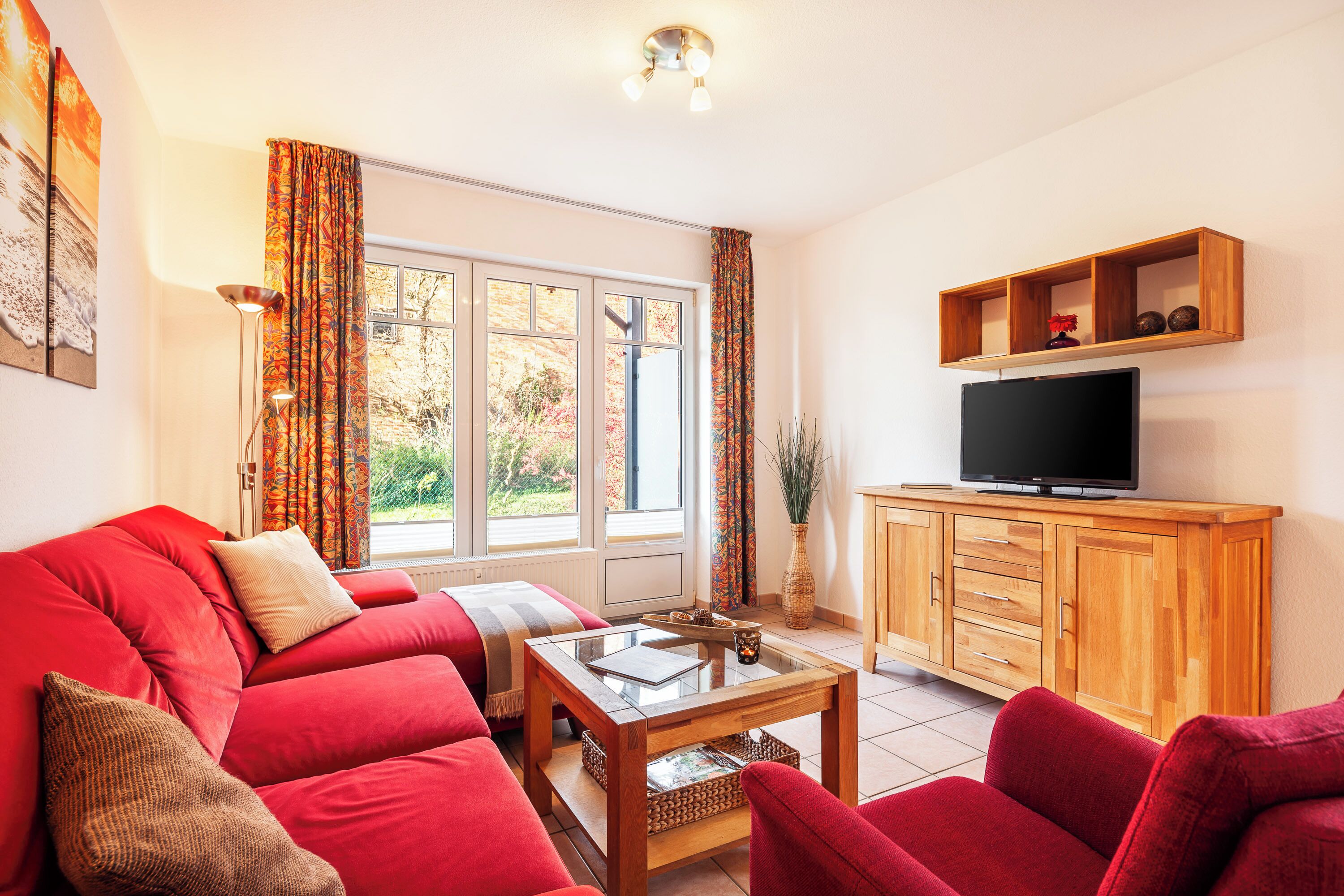 A living room with a red sofa, a wooden coffee table, and a TV on a wooden cabinet.
