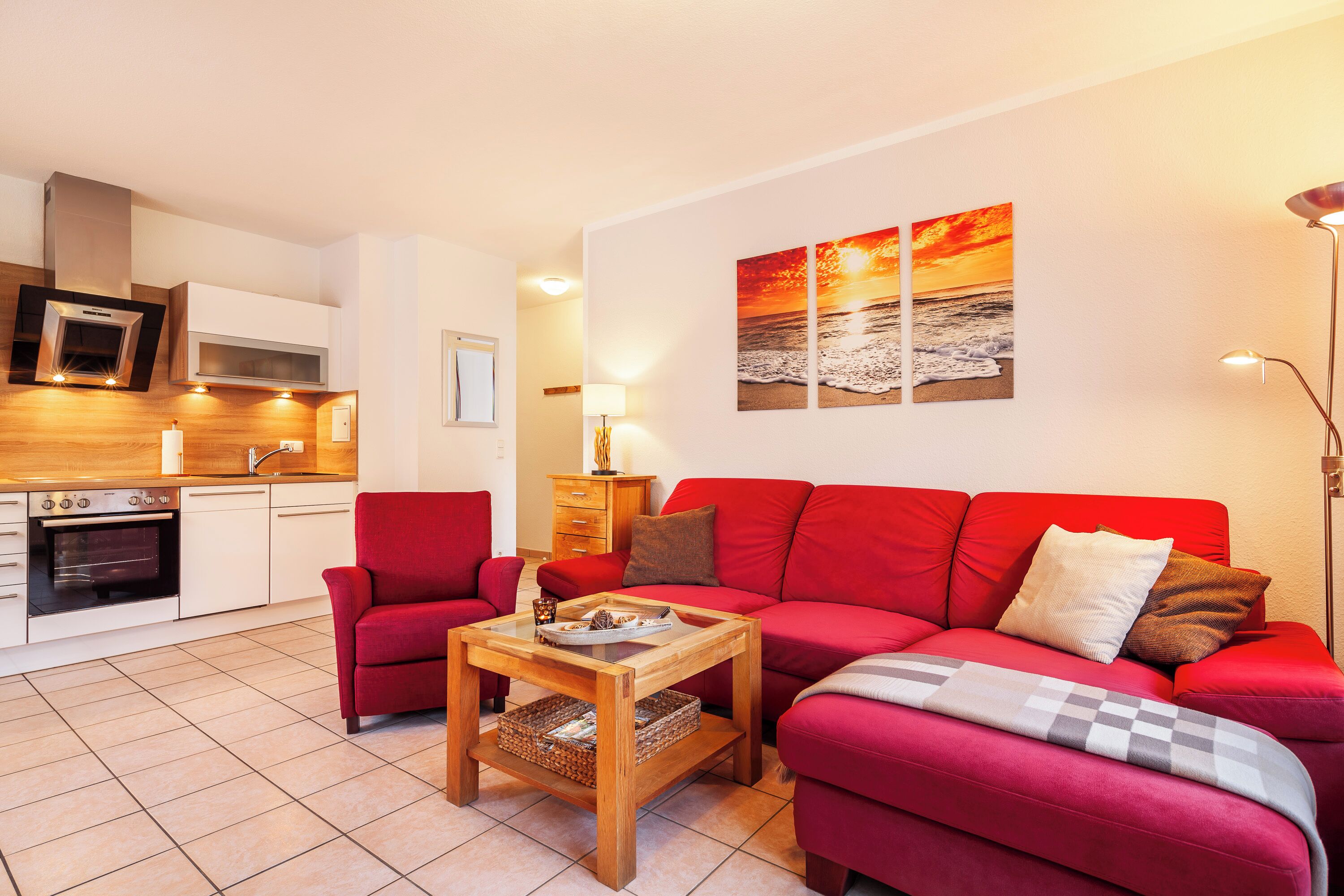 A modern living room with a red sofa, a wooden coffee table, and a kitchen area with white cabinets and a microwave.