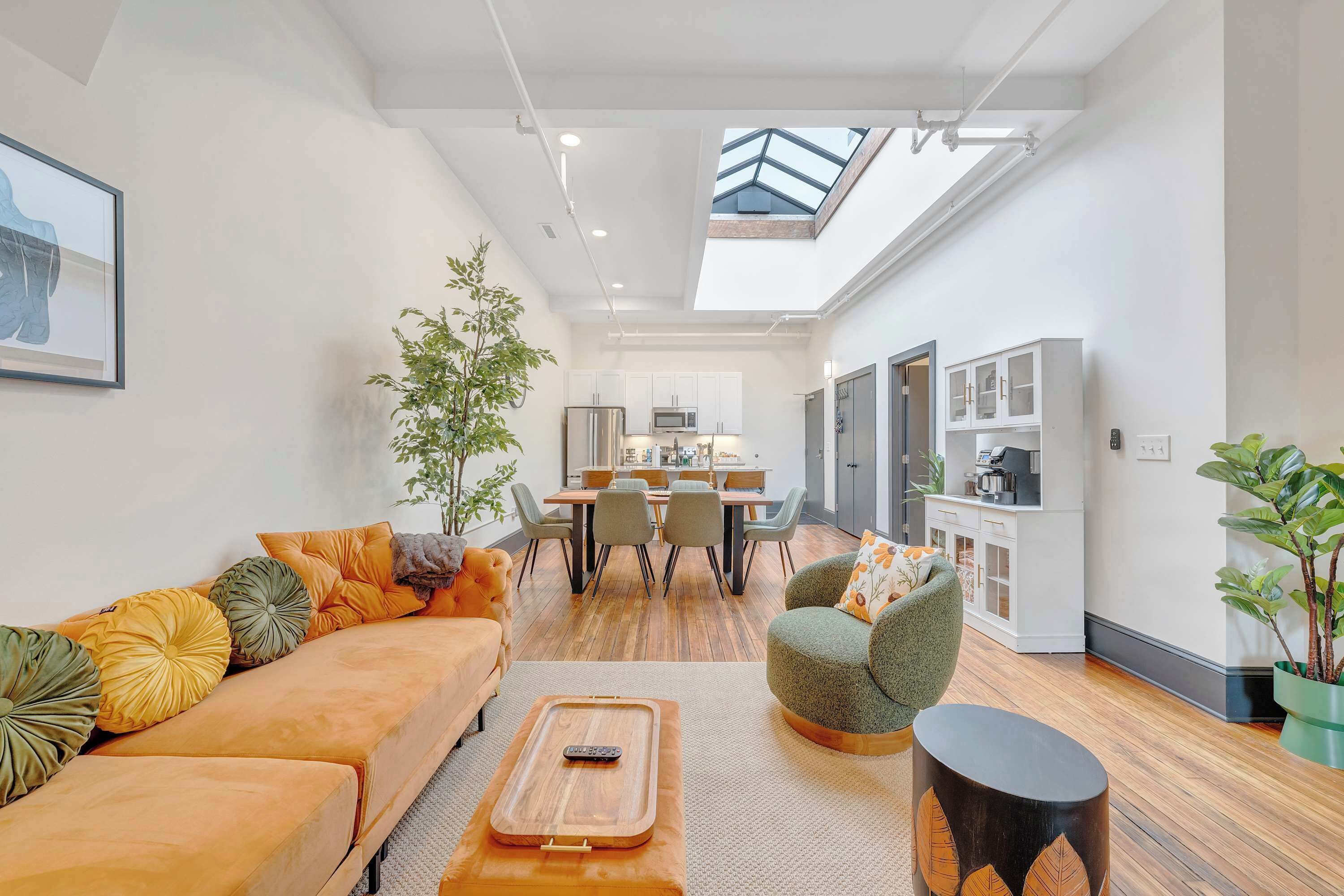 Un salon moderne comprenant un canapé, un fauteuil et une table basse, un coin repas avec des chaises et une table, et une cuisine équipée de placards et d’appareils électroménagers.