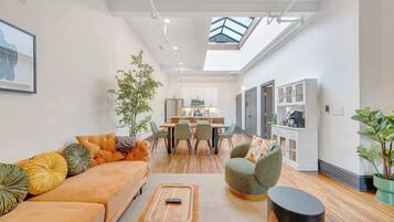 Un salon moderne comprenant un canapé, un fauteuil et une table basse, un coin repas avec des chaises et une table, et une cuisine équipée de placards et d’appareils électroménagers.
