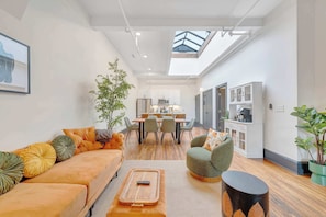 Ein modernes Wohnzimmer mit Sofa, Sessel und Couchtisch, ein Essbereich mit Stühlen und Tisch sowie eine Küche mit Schränken und Geräten.