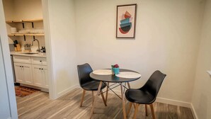 Ein Essbereich mit einem runden Tisch, zwei schwarzen Stühlen und einem gerahmten, abstrakten Gemälde an der Wand.