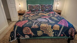 Ein Bett mit einem grün gepolsterten Kopfteil, zwei Nachttische mit Lampen und einer zudeckenden Bettdecke mit Blumenmuster.