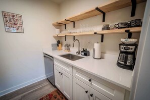Een keuken met witte kasten, een roestvrijstalen spoelbak, houten planken en een koffiezetapparaat.