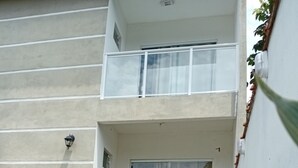 Ein modernes, zweistöckiges Gebäude mit Balkon, Glastür und einem kleinen Gartenbereich mit trittfesten Steinen und Pflanzen.