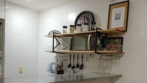 Eine Küche mit einer Mikrowelle, Regalen mit Gläsern und Küchenutensilien sowie zwei Barhocker.