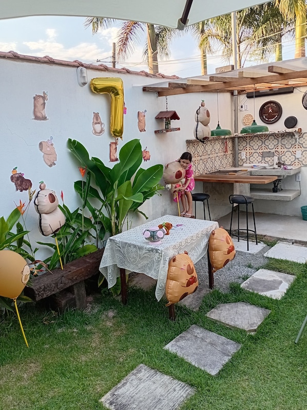 Un patio con una mesa dispuesta para comer, rodeado de adornos con forma de animales, un globo grande con el número uno y diversas plantas.