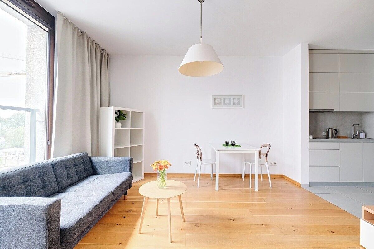 Un salon moderne avec un canapé, une petite table ronde ornée d’un vase et un coin repas avec des chaises.