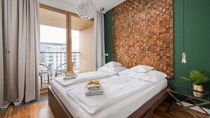 A modern hotel room with a large bed, a wooden wall panel, a balcony with a view, and a small side table with a plant. - I need the message to rewrite! Please share the full text. (Warsaw)