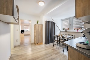 Une cuisine moderne avec des meubles en bois, un coin repas comprenant une table et des chaises, et une fenêtre équipée de stores.