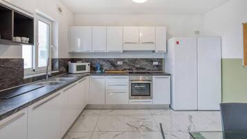Una cucina moderna con mobili bianchi, un forno a microonde integrato, un forno e un frigorifero.