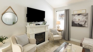 A living room with a fireplace, a television mounted above it, a round mirror, and a framed artwork on the wall.