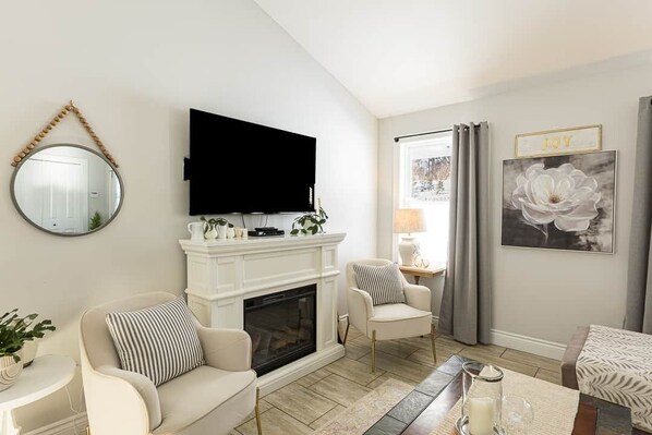 A living room with a fireplace, a television mounted above it, a round mirror, and a framed artwork on the wall.