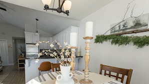 A dining area with a table set for two, a vase with flowers, and a chandelier.