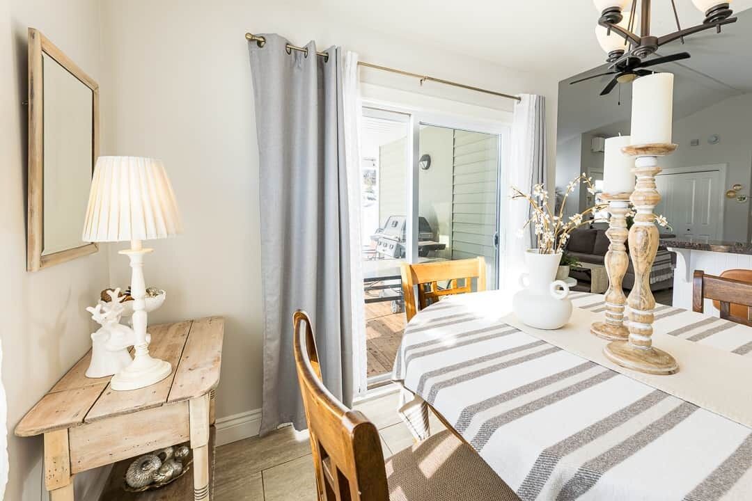 Un coin repas avec une table dressée pour deux personnes, une petite table en bois avec une lampe et un grand miroir au mur.