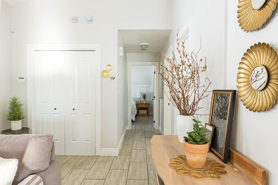 Un couloir avec une porte blanche, un banc en bois agrémenté d’une plante et des œuvres d’art décoratives accrochées au mur.