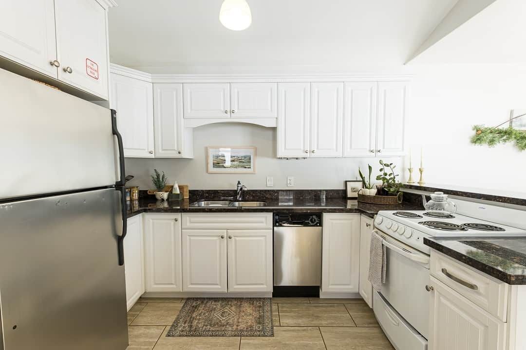 A kitchen with white cabinets, a stainless steel refrigerator, a dishwasher, a stove, and a sink.