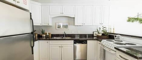 A kitchen with white cabinets, a stainless steel refrigerator, a dishwasher, a stove, and a sink.