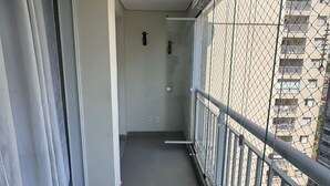 Ein schmaler Balkon mit Metallgeländer, einer Schiebeglastür und Blick auf ein Gebäude mit mehreren Balkonen.
