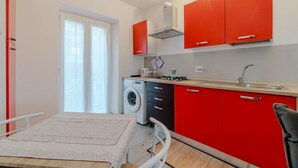 A compact kitchen with red cabinets, a washing machine, and a dining area with a table. - GuestHost - A cozy 40 sq m apartment that comfortably accommodates two people, located on the third floor of a period building with an elevator. The apartment is centrally located in the Quadrilatero neighborhood, just steps from Piazza della Consolata a (Turin)