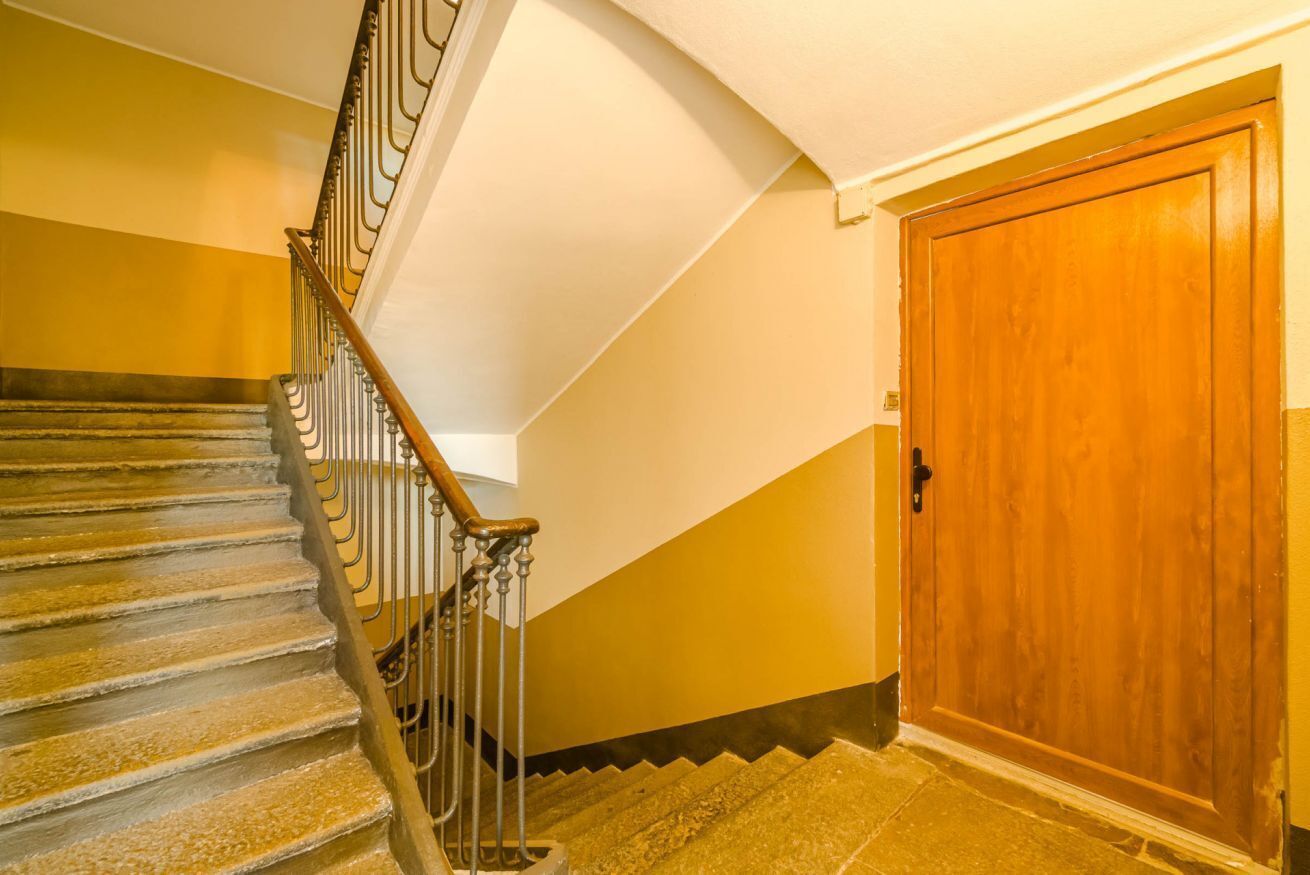 Una scala con ringhiera in legno e balaustre metalliche, che conduce a una porta in legno.