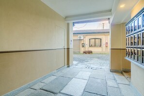 Ein Korridor mit Steinböden, beigen Wänden und Blick auf ein Gebäude mit Fenster und Tür.