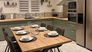A modern kitchen with a dining area. It includes a wooden dining table set with plates, glasses, and a centerpiece. There are cabinets, a refrigerator, and an oven in the kitchen. - Spacious house near the lake - 6 people (Saint-Épain)